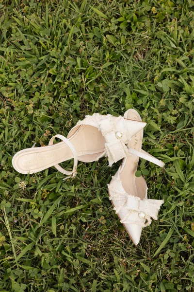 Bridal shoes featuring a graceful bow detail, heels arranged neatly on a grass lawn in an outdoor wedding setting.