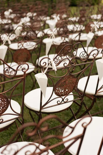 Ceremony chair decor featuring petal toss cones along outdoor ceremony seating on a grass lawn bordered by lush garden greenery.