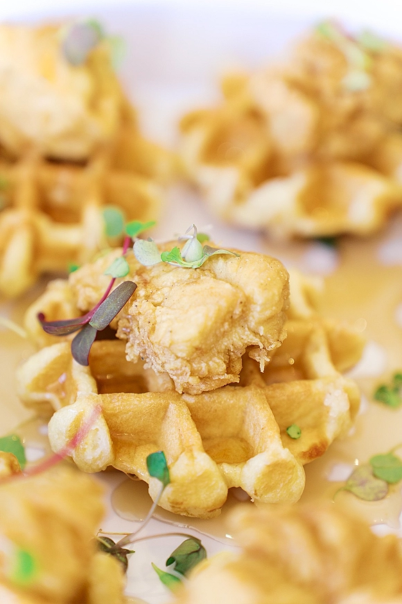 Chicken and waffles wedding brunch menu bites stacked with crispy fried chicken and microgreens on a white plate with syrup drizzle