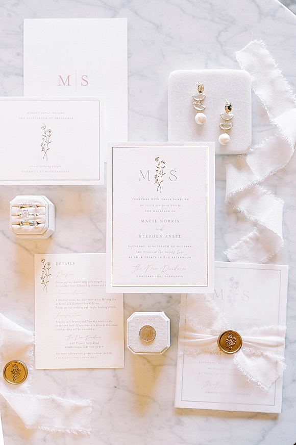 Invitation suite minimal wedding invitation suite arranged with RSVP card, rings, pearl drop earrings, wax seals and ribbon on marble surface
