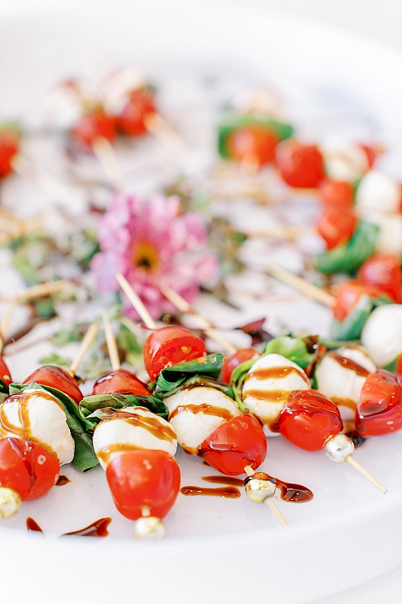 Wedding appetizer skewers, caprese skewers with cherry tomatoes, mozzarella, basil and balsamic glaze on pearl-ended picks on a white platter
