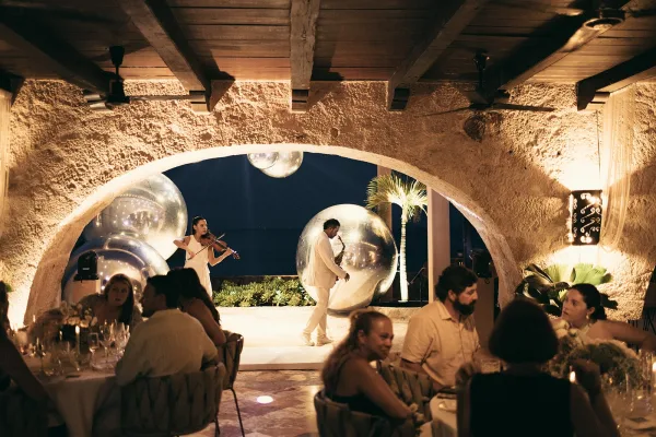 Wedding reception entertainment with live wedding music by a violinist under a stone arch, set against an ocean night sky and silhouetted palms.
