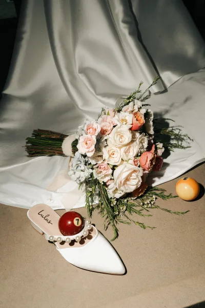 Bouquet close-up of a white and blush bridal bouquet resting on satin fabric, with a single bridal shoe framing the delicate blooms.