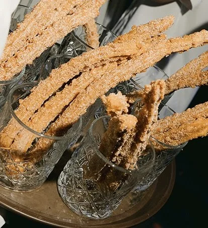 Wedding churros at a churro bar, neatly arranged in cut crystal glassware, the sticks inviting guests to grab a sweet, handheld bite.