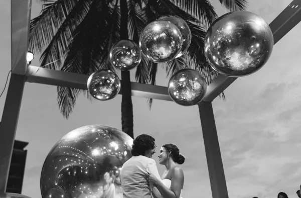 First dance at an outdoor wedding dance as the bride and groom twirl under shimmering disco balls, a palm tree silhouetted against dusk.