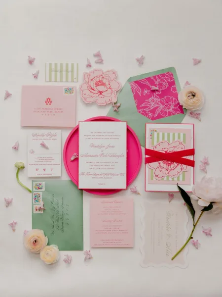 Wedding invitation suite with pink wedding invitations, RSVP and save-the-date cards, ribbon and vintage stamps on a white backdrop