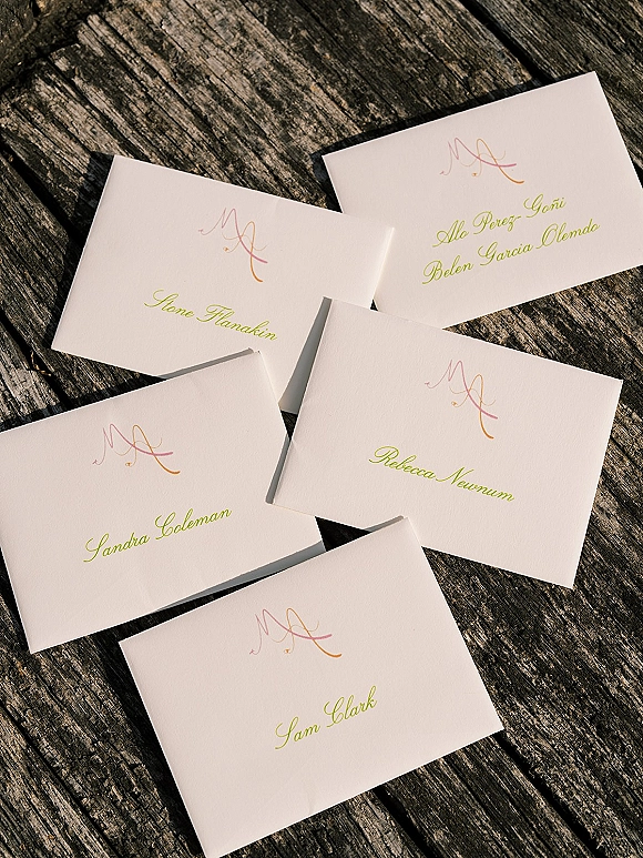 Wedding place cards with calligraphy place cards and monogram details on white cardstock with envelopes on a weathered wood table