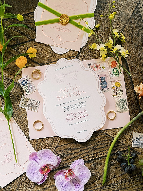 Invitation suite wedding invitation flat lay with deckle edge cards, wax seal, green velvet ribbon, vintage stamps, rings, and orchids on wood table