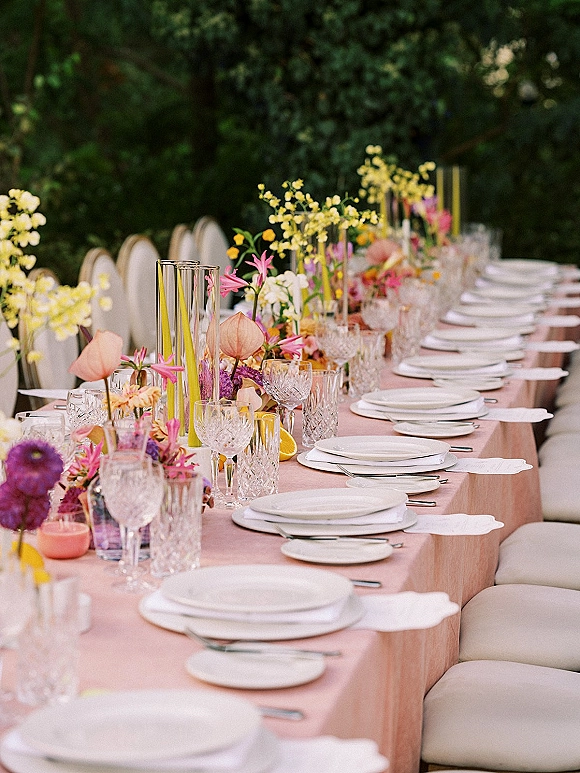 Reception tablescape with pink wedding tablescape linens, floral centerpieces, crystal glassware, taper candles, and citrus slices in a garden setting