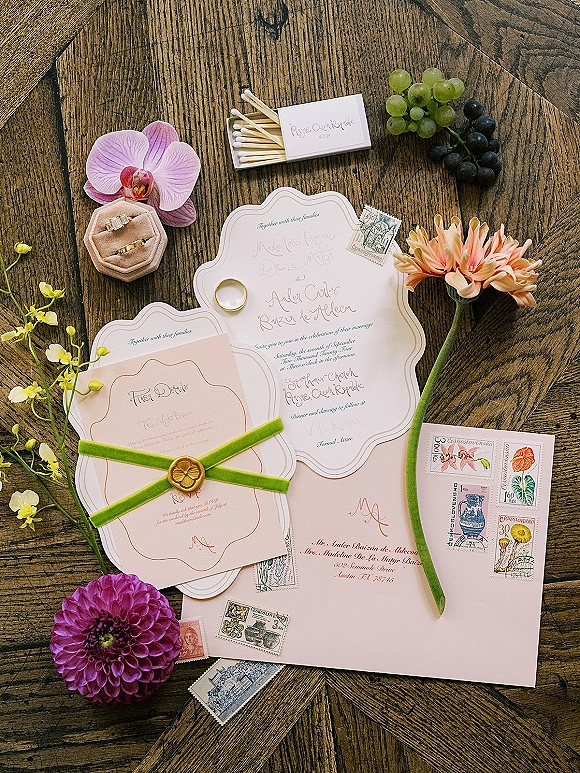 Invitation suite wedding invitation flat lay with wax-sealed envelope, velvet ribbon, rings, and orchid blooms on a wood table