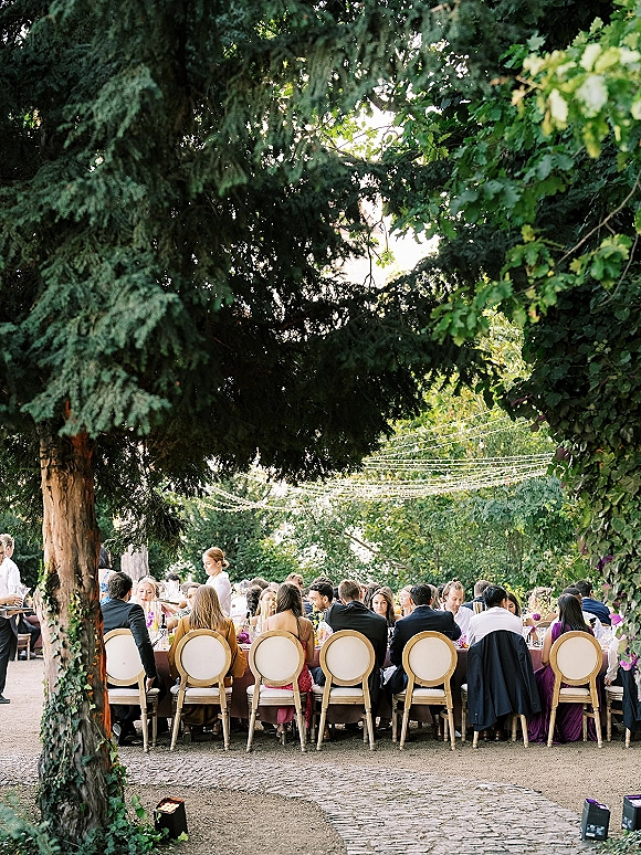 Wedding reception with outdoor wedding dinner setup featuring a long banquet table, floral centerpieces, and string lights under trees