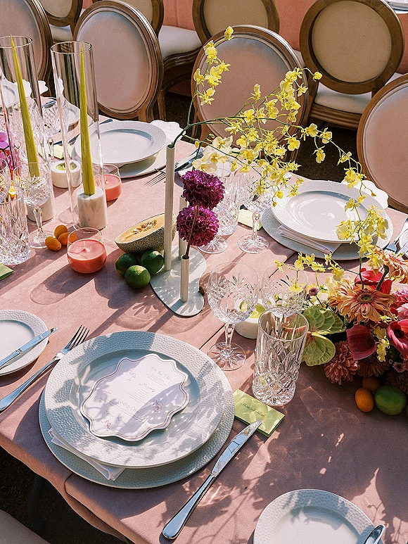 Reception tablescape with pink wedding table decor, yellow orchid and dahlia centerpiece, tall taper candles, crystal stemware, citrus accents in sunlight