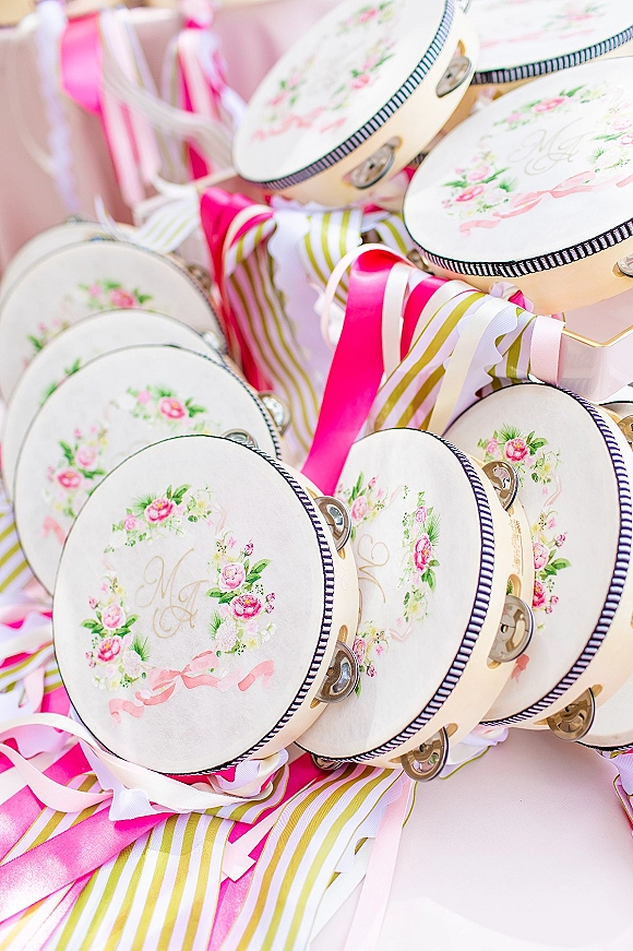 Wedding favors with personalized tambourines featuring floral monogram and pink satin ribbons, arranged on a soft pink backdrop