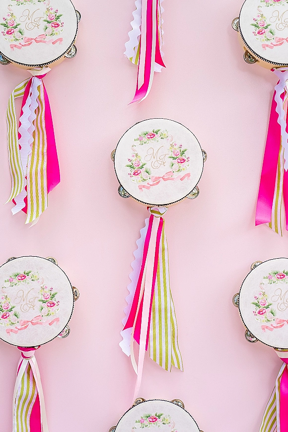 Wedding favor idea featuring personalized wedding favors tambourines with floral monogram decals and hot pink ribbon streamers on a pink backdrop