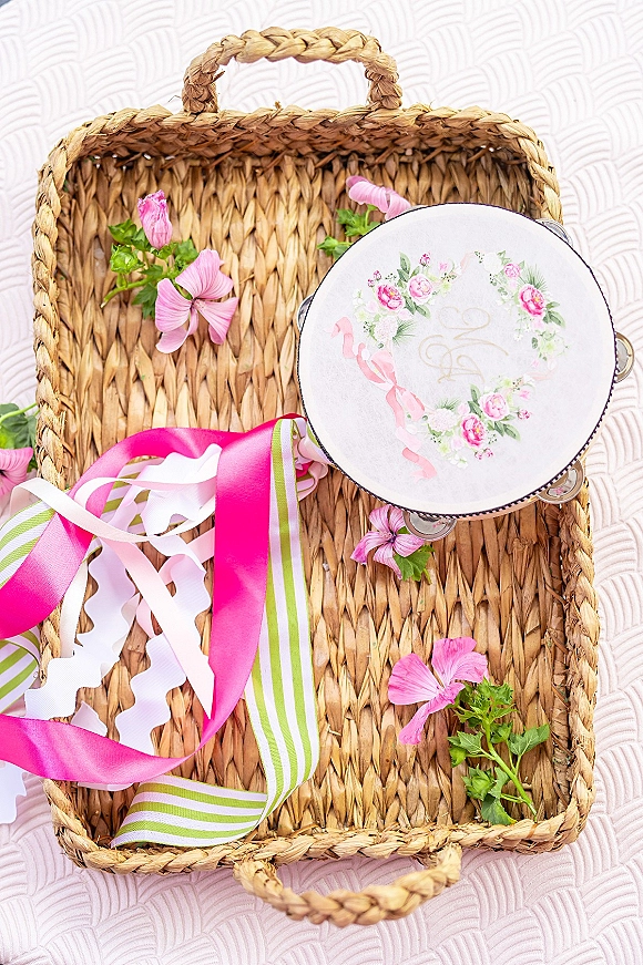 Wedding invitation suite with pink wedding stationery, satin ribbon and pink flowers beside a woven straw basket on a textured white surface