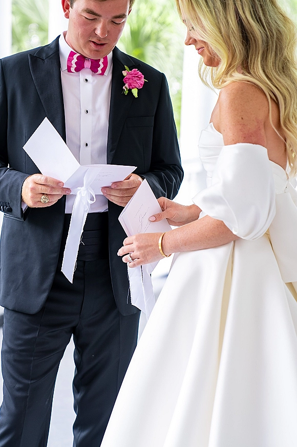 Wedding vow letters in vow cards and envelopes with ribbon, bride’s ring and groom’s pink bow tie in bright window light with greenery