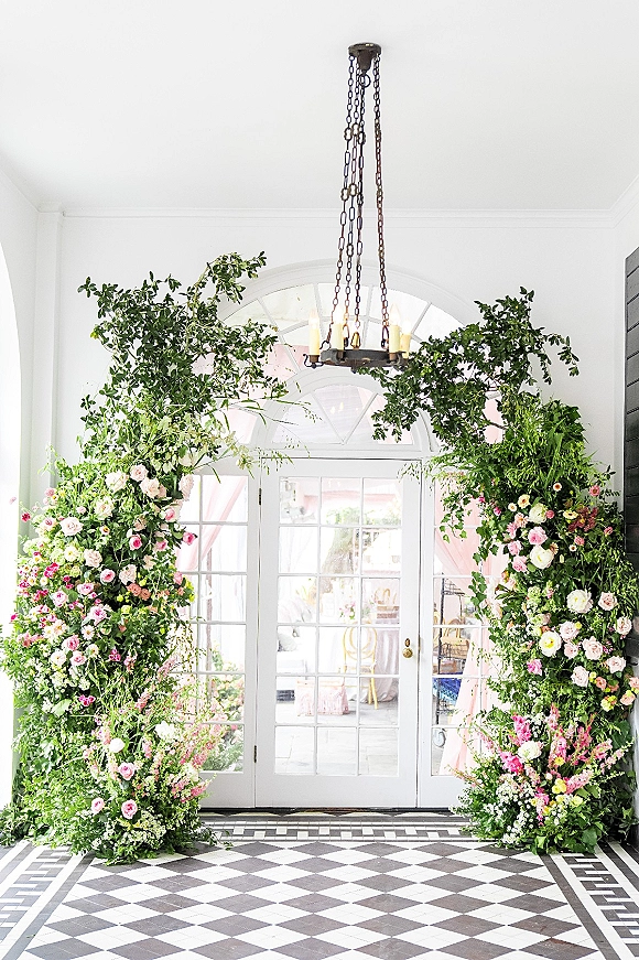 Floral arch decor at a wedding entrance floral arch with greenery and roses framing glass double doors in a white tiled entryway