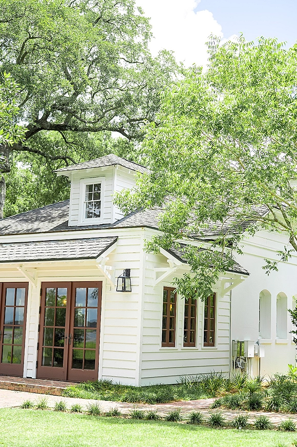 Wedding venue exterior with white chapel exterior details, French doors and lantern light opening onto a brick walkway framed by trees