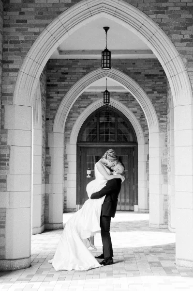 Wedding couple portrait of groom dipping the bride for a kiss, her long train and veil flowing beneath lantern-lit stone archway doors