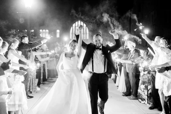 Sparkler exit with newlyweds running hand in hand through a wedding send off tunnel of guests under night sky and smoky lamplight
