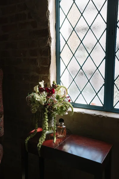 Bridal bouquet, a calla lily bouquet with cascading greenery, rests on a stone windowsill beneath a leaded glass window