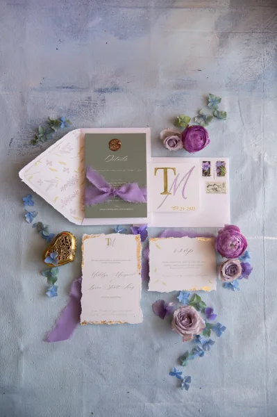 Invitation suite wedding invitation flat lay with wax seal and silk ribbon, deckled cards, stamps, and floral petals on blue surface