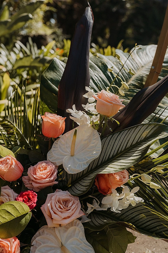 Wedding floral arrangement with tropical wedding flowers, peach and blush roses and white anthurium, set in sunlit garden greenery