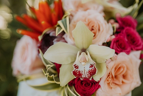 Wedding bouquet with orchid blooms and peach roses, mixed florals and greenery, photographed close up against a soft blurred background