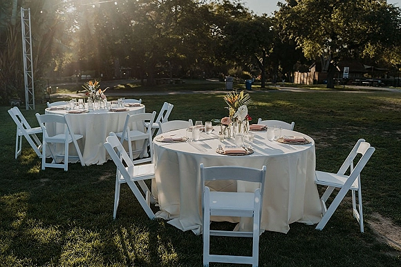 Outdoor reception tablescape with round wedding reception tables, white tablecloths, bud vase florals and votive candles on a sunlit lawn