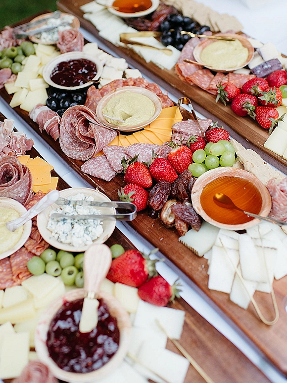 Charcuterie board wedding cocktail hour food with cheeses, salami, prosciutto, olives, berries, jam, honey and crackers on white tablecloth