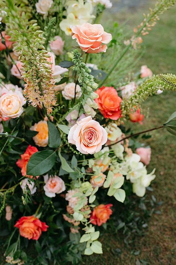 Wedding florals with rose wedding flowers in peach and coral roses, lush greenery and buds arranged on a grass lawn in a garden setting