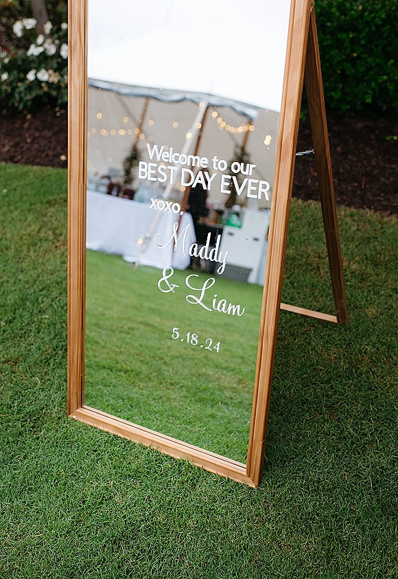 Wedding welcome sign mirror wedding welcome sign on an easel, full-length wooden-framed mirror with vinyl lettering under string lights by a tent
