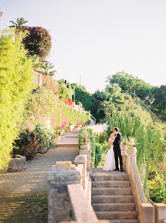 Couple portrait of bride in a strapless wedding dress and groom in a black suit embracing on a stone staircase in a cactus garden setting