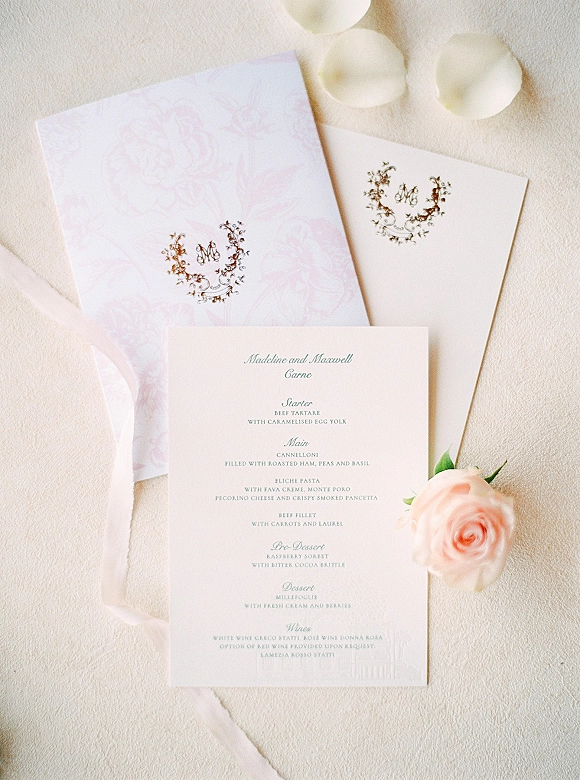 Wedding invitation suite with wedding menu card and monogram crest, blush rose accent, envelopes and wax seals on light textured fabric