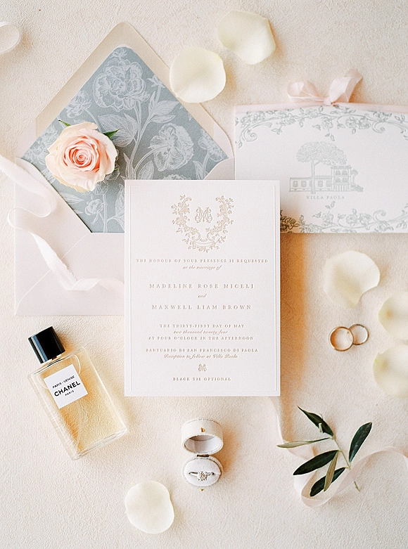 Wedding invitation suite flat lay with envelope liner, wax seal, ribbon, rose petals, rings and perfume on linen fabric backdrop