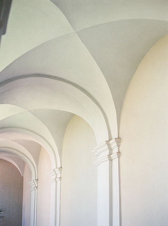 Arched hallway with arched corridor perspective, white walls and soft natural light highlighting columns, molding, and ceiling arches
