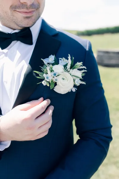 Groom boutonniere with blue and white blooms, pinned neatly to a navy suit, highlighting a classic formal look.