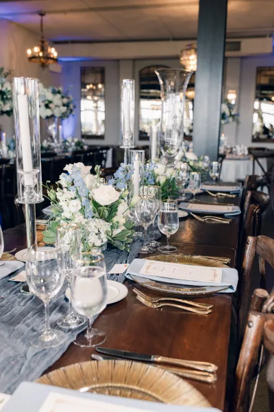 Reception tablescape featuring long banquet table decor with a blue table runner beneath sparkling chandeliers and mirrors.