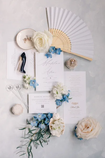 Wedding invitation suite with blue and white invitations styled alongside a ring box, showcasing elegant script and coordinated pieces.
