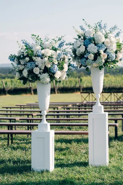 Ceremony flowers anchor lush altar flower arrangements with hydrangeas on a grass lawn, backed by vineyard rows and distant hills.