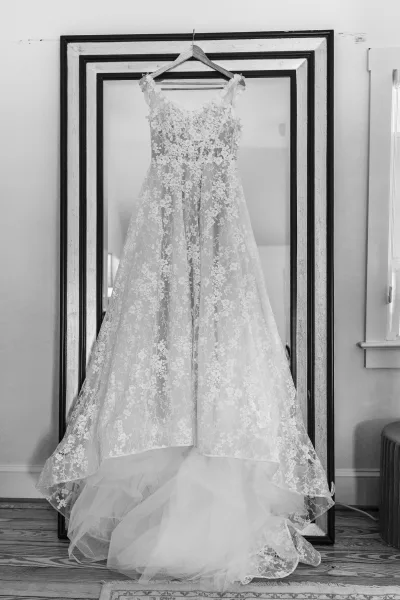 Wedding dress, a lace bridal gown beside a mirror, its airy layers falling toward the wood floor and area rug