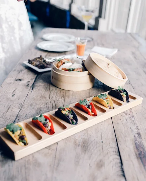 Wedding appetizers featuring mini taco appetizers arranged neatly on a rustic wood table, set before a softly blurred dining area.