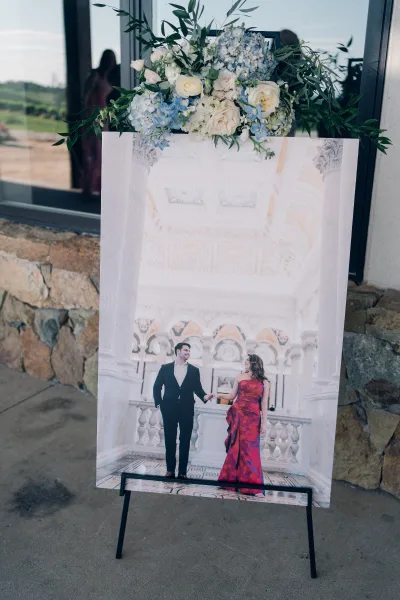 Wedding signage as a photo welcome sign mounted on an easel, set by a glass window and stone wall with views of the surrounding outdoor landscape.