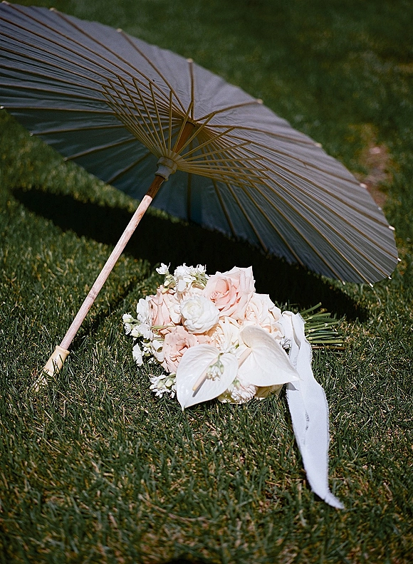 Bridal bouquet with blush rose bouquet and white anthurium blooms, tied with long ribbon, resting on a grass lawn