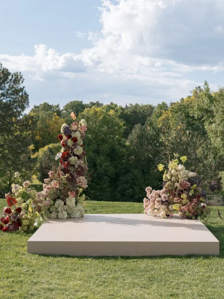 Ceremony altar decor with outdoor wedding altar flowers, lush roses, hydrangeas, greenery, and anthuriums on a lawn under cloudy sky