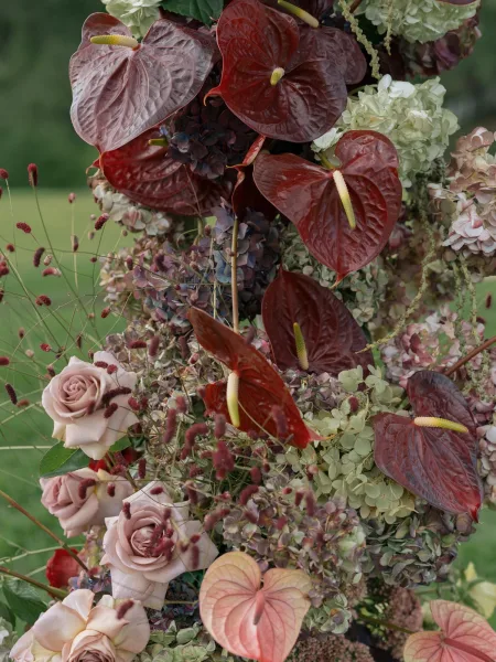 Wedding floral arrangement featuring anthurium wedding flowers with roses, hydrangea and hanging amaranthus against a blurred green lawn backdrop