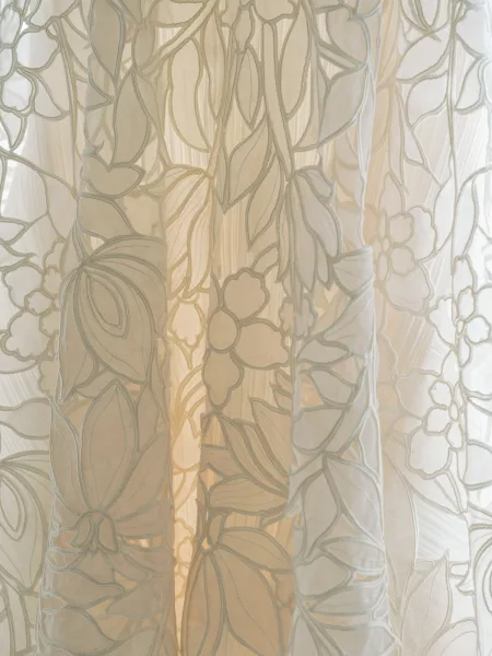 Lace wedding dress with floral lace and embroidered appliqué on sheer tulle, highlighted by soft window light and visible seam stitching