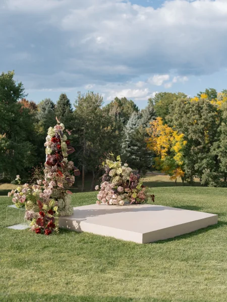 Ceremony altar decor with outdoor wedding altar featuring lush roses, hydrangea and anthurium on a white platform on a grassy lawn under cloudy sky