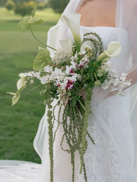 Bridal bouquet with cascading bridal bouquet of calla lilies, orchids, anthurium and greenery, trailing amaranthus against soft lawn backdrop