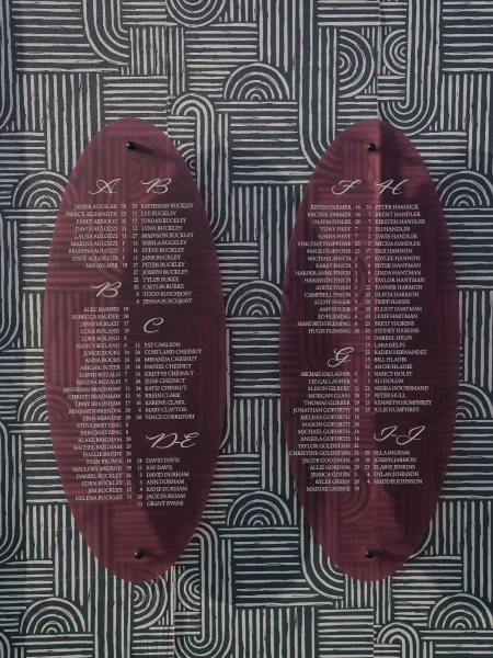Seating chart sign on burgundy acrylic panels with white calligraphy, standoff mounted against a bold black-and-white geometric wall